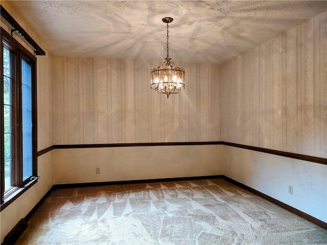 carpeted empty room with a chandelier, a textured ceiling, and baseboards