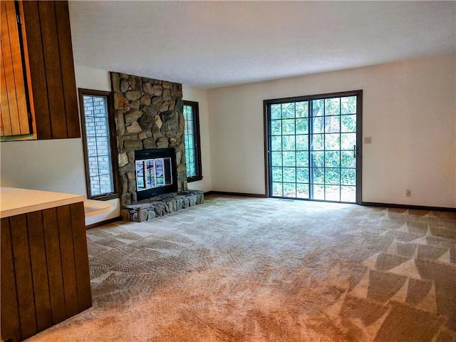 unfurnished living room featuring carpet floors, baseboards, and a stone fireplace