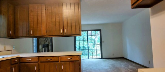 kitchen featuring light countertops, carpet flooring, brown cabinets, and baseboards