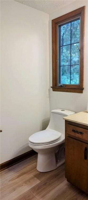 half bathroom featuring wood finished floors, toilet, vanity, and baseboards