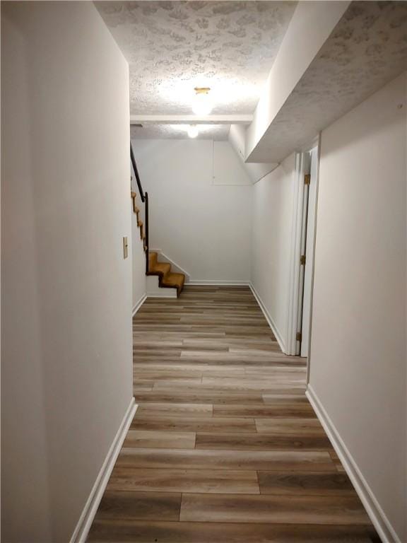 corridor with light wood-style flooring, baseboards, a textured ceiling, and stairs