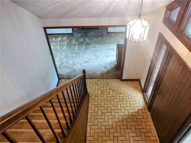 stairs featuring a chandelier, a textured ceiling, brick patterned flooring, baseboards, and carpet floors