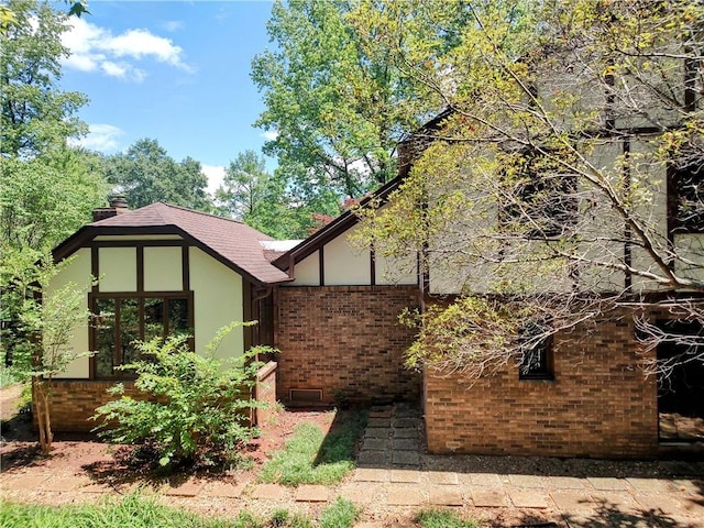 view of property exterior featuring brick siding, a chimney, roof with shingles, and stucco siding