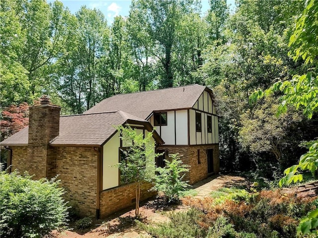 view of property exterior featuring brick siding, roof with shingles, a chimney, and board and batten siding