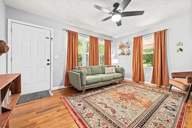 living area featuring light wood finished floors, plenty of natural light, a ceiling fan, and a textured ceiling