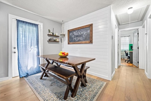 dining space featuring attic access, light wood-style floors, a textured ceiling, an office area, and baseboards