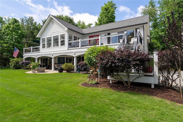 back of house with a balcony, a patio, a lawn, and roof with shingles