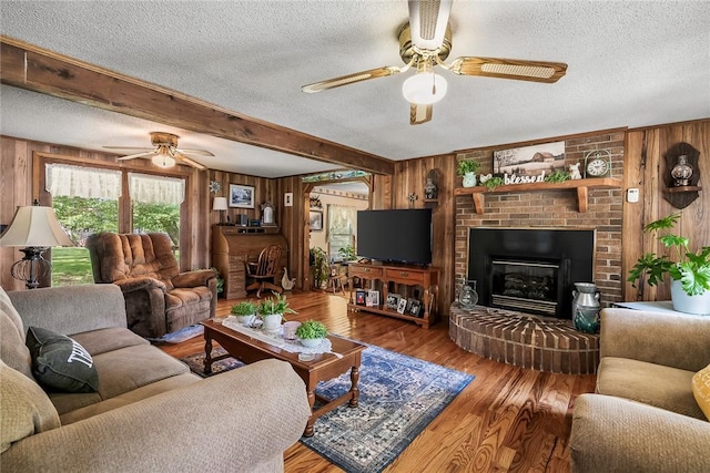 living area with ceiling fan, wooden walls, a textured ceiling, a fireplace, and wood finished floors