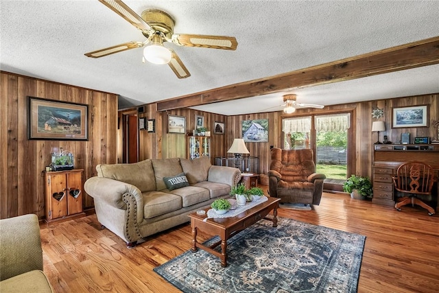 living area featuring a ceiling fan, wood walls, a textured ceiling, wood finished floors, and beam ceiling