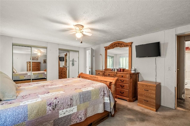 carpeted bedroom featuring two closets, a ceiling fan, and a textured ceiling