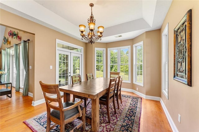 dining area with light wood-style flooring, french doors, a chandelier, baseboards, and a tray ceiling