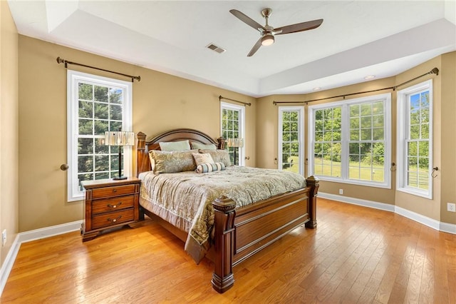 bedroom featuring a tray ceiling, baseboards, light wood-style flooring, and multiple windows