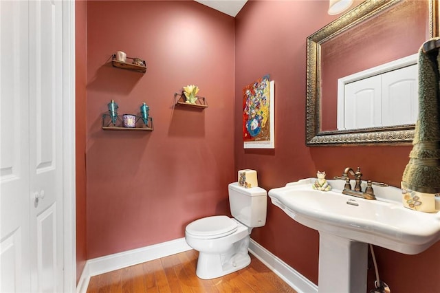 half bath featuring baseboards, toilet, wood finished floors, and a sink