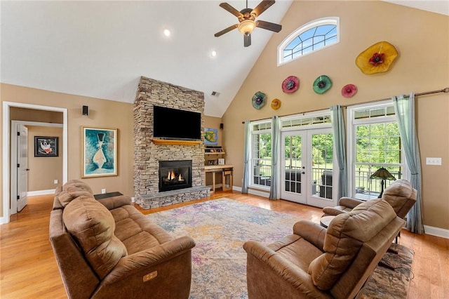 living room featuring high vaulted ceiling, a ceiling fan, baseboards, a stone fireplace, and light wood finished floors