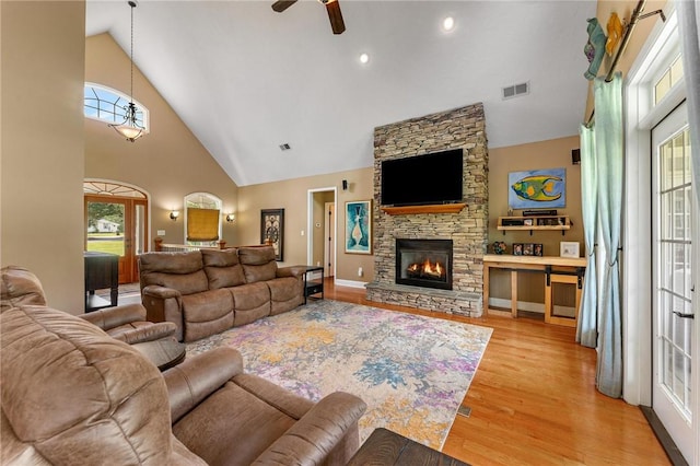living room with wood finished floors, a ceiling fan, high vaulted ceiling, and a stone fireplace