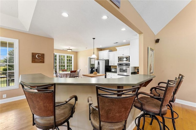 kitchen featuring appliances with stainless steel finishes, baseboards, light wood-type flooring, white cabinets, and a peninsula