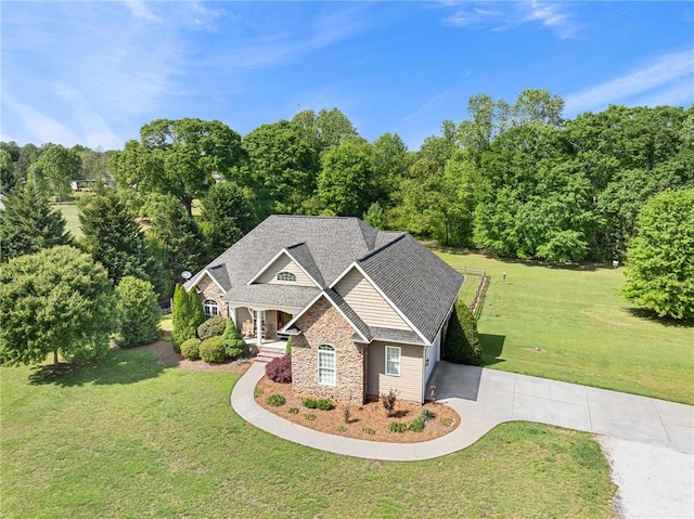 view of front of home with concrete driveway, a front yard, stone siding, and a shingled roof