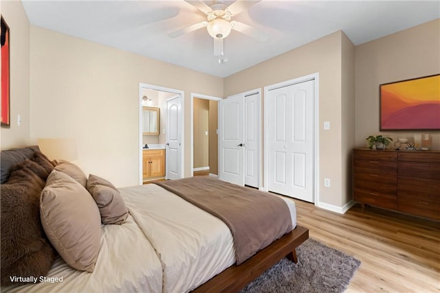 bedroom featuring two closets, light wood-style floors, baseboards, ensuite bathroom, and a ceiling fan