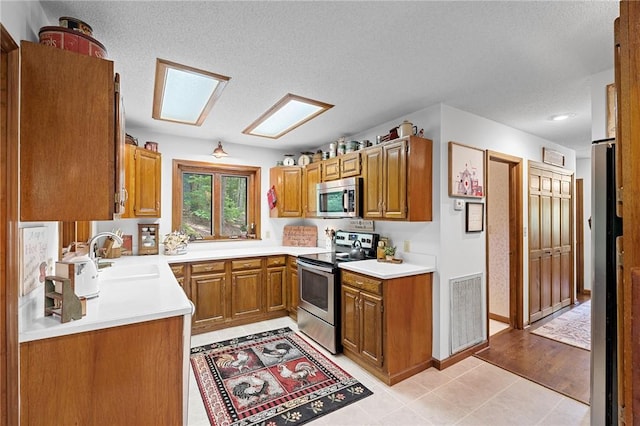 kitchen featuring stainless steel appliances, a sink, brown cabinets, light countertops, and a textured ceiling