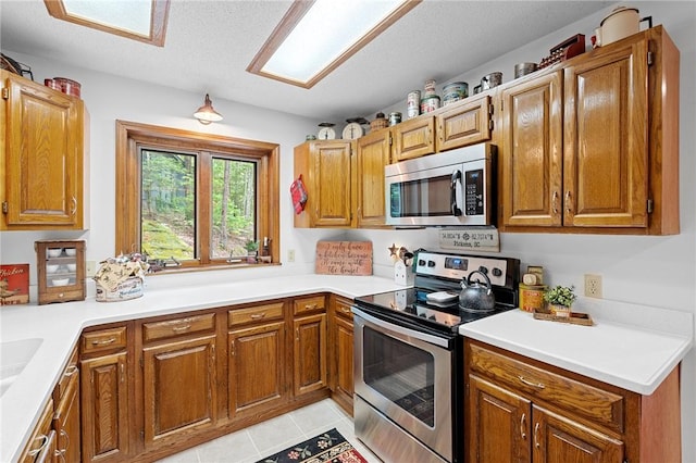 kitchen with stainless steel appliances, light tile patterned floors, brown cabinetry, and light countertops