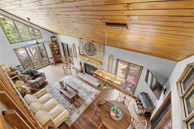 living room featuring wooden ceiling, vaulted ceiling, a stone fireplace, and wood finished floors