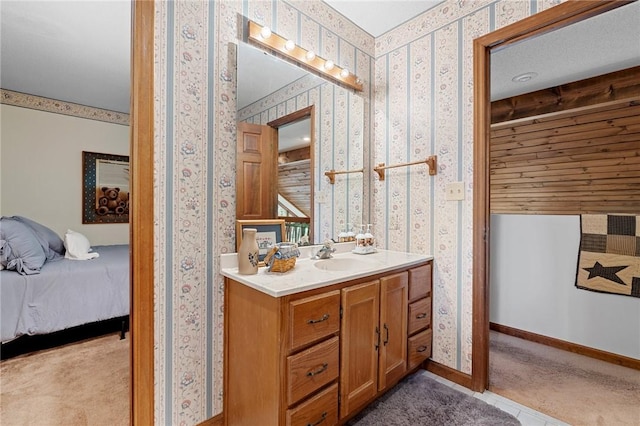 ensuite bathroom featuring wallpapered walls, vanity, and baseboards