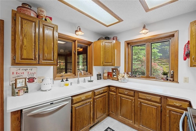kitchen featuring stainless steel dishwasher, brown cabinets, light countertops, range, and a sink