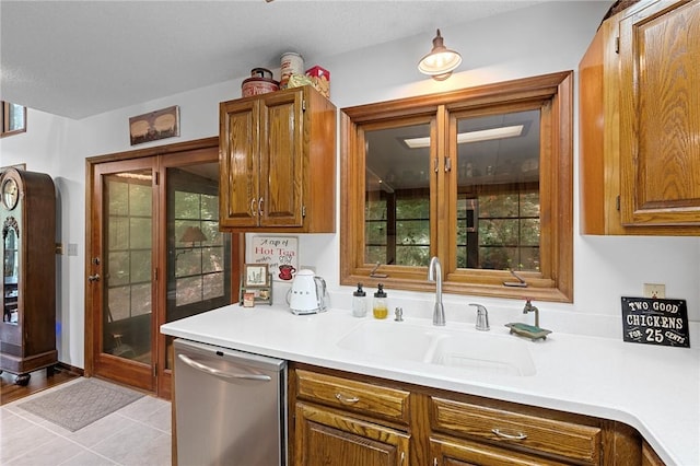 kitchen with stainless steel dishwasher, brown cabinets, light countertops, and a sink