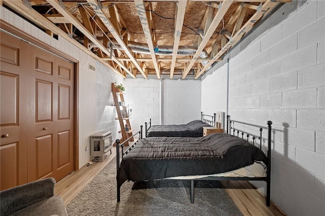 bedroom with light wood-style floors, heating unit, and concrete block wall