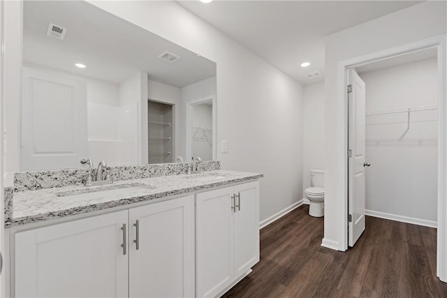 full bath with toilet, wood finished floors, baseboards, double vanity, and a walk in closet