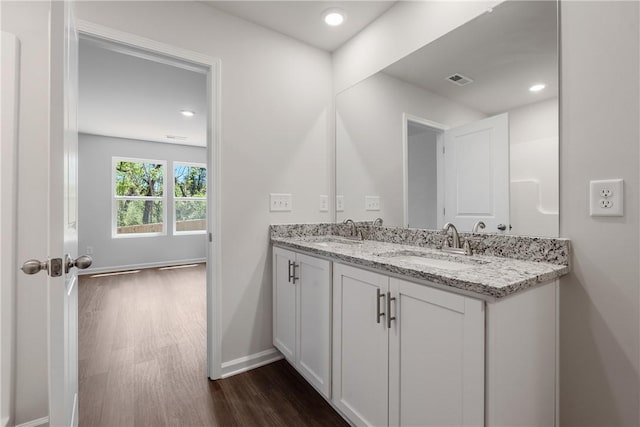 bathroom featuring wood finished floors, baseboards, double vanity, and recessed lighting