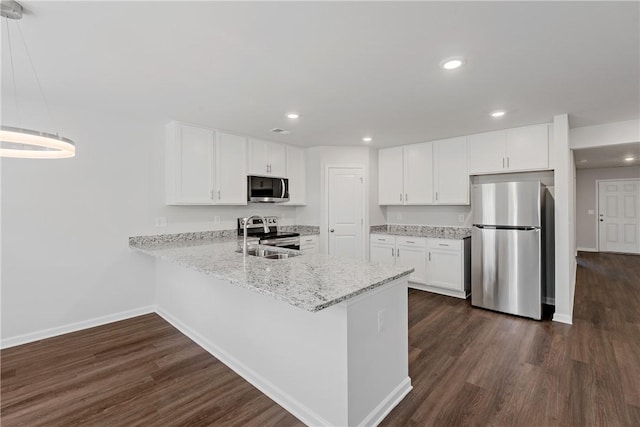 kitchen featuring appliances with stainless steel finishes, baseboards, a sink, dark wood-style flooring, and a peninsula