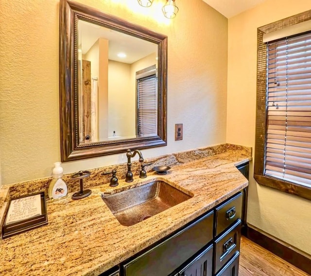 bathroom featuring vanity, a textured wall, baseboards, and wood finished floors