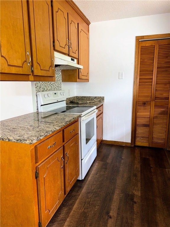 5265 Slater Rd, Anderson, SC 29621 - kitchen with white range with electric stovetop, under cabinet range hood, dark wood-type flooring, brown cabinetry, and light stone counters