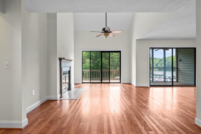 704 Loran Pointe Cir, Seneca, SC 29672 - unfurnished living room featuring wood finished floors, ceiling fan, baseboards, a towering ceiling, and a glass covered fireplace