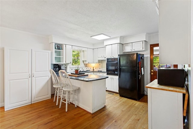125 Brookwood Rd, Seneca, SC 29678 - kitchen featuring black appliances, a peninsula, light wood-type flooring, a textured ceiling, and a kitchen breakfast bar