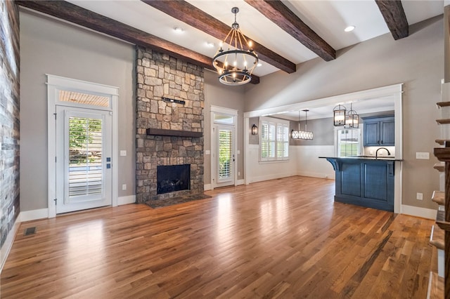 1219 Old Mill Rd, Easley, SC 29642 - unfurnished living room featuring a chandelier, plenty of natural light, a stone fireplace, wood finished floors, and beamed ceiling
