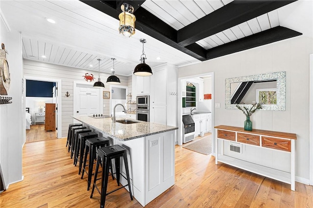 1047 Tranquility Ln, Hartwell, GA 30643 - kitchen with stainless steel microwave, light wood-type flooring, a center island with sink, a wooden ceiling with exposed beams, and wooden walls
