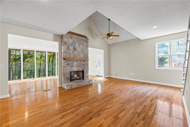 168 Wilderness Pt, Hartwell, GA 30643 - unfurnished living room featuring ceiling fan, hardwood / wood-style floors, plenty of natural light, a textured ceiling, and a stone fireplace