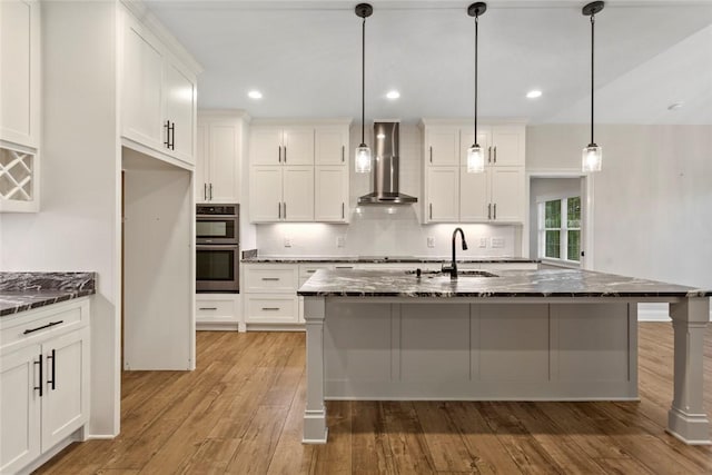 340 Fiddlers Way, Seneca, SC 29678 - kitchen with wall chimney exhaust hood, double oven, light wood-style floors, dark stone counters, and white cabinetry