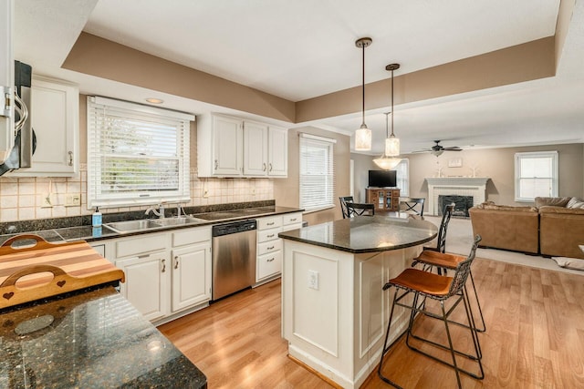 kitchen featuring a kitchen breakfast bar, sink, hanging light fixtures, stainless steel dishwasher, and white cabinetry