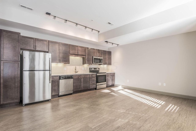 kitchen featuring stainless steel appliances, tasteful backsplash, light hardwood / wood-style floors, track lighting, and dark brown cabinets