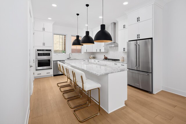 kitchen featuring appliances with stainless steel finishes, a kitchen island, wall chimney exhaust hood, and white cabinetry