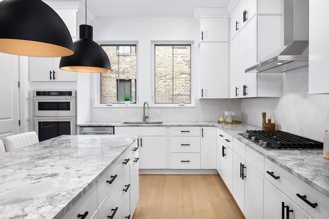 kitchen with sink, wall chimney range hood, white cabinetry, and hanging light fixtures