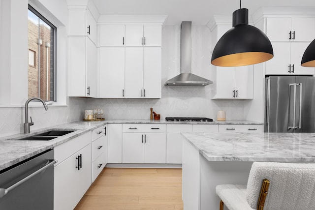 kitchen featuring wall chimney exhaust hood, stainless steel appliances, pendant lighting, sink, and white cabinetry