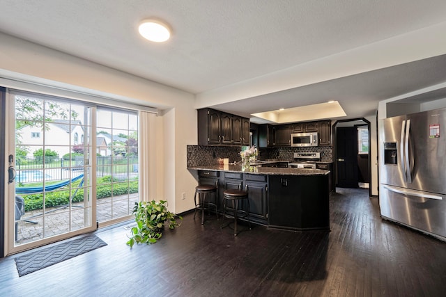 12627 Oakmere Dr, Pickerington, OH 43147 - kitchen with stainless steel appliances, dark wood-style floors, a peninsula, decorative backsplash, and a tray ceiling