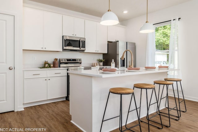 344 Postle Blvd, Columbus, OH 43228 - kitchen featuring white cabinetry, wood finished floors, stainless steel appliances, a center island with sink, and a breakfast bar area