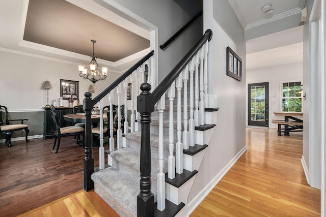 stairs featuring wood finished floors, ornamental molding, baseboards, and a notable chandelier