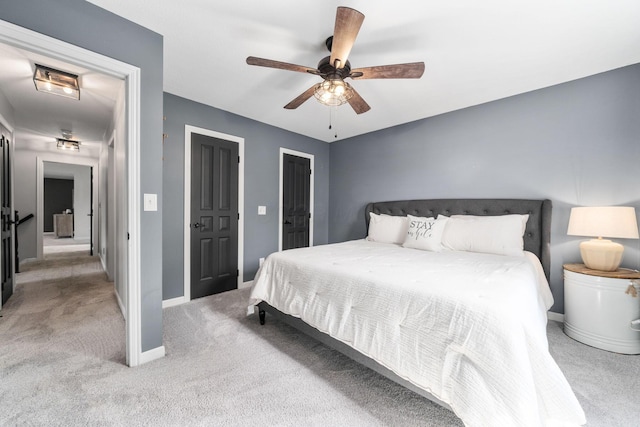 bedroom with light colored carpet, ceiling fan, baseboards, and two closets
