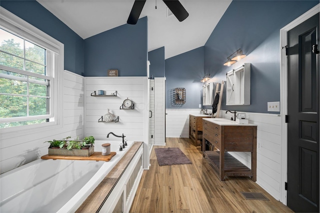 bathroom with a shower stall, a wainscoted wall, vaulted ceiling, a ceiling fan, and a bath